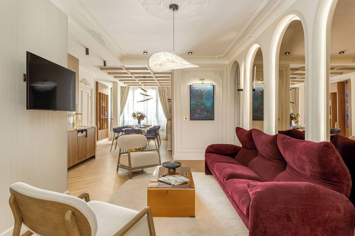 A spacious living room with a red velvet sofa, a wooden coffee table, and a flat-screen TV mounted on the wall.