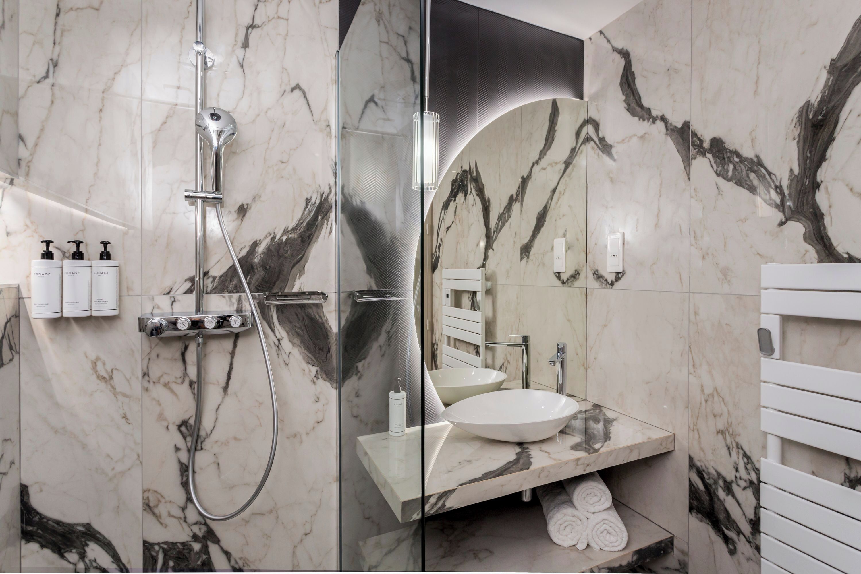 A modern bathroom with a glass-enclosed shower, a white sink with a marble countertop, and a towel rack with towels.