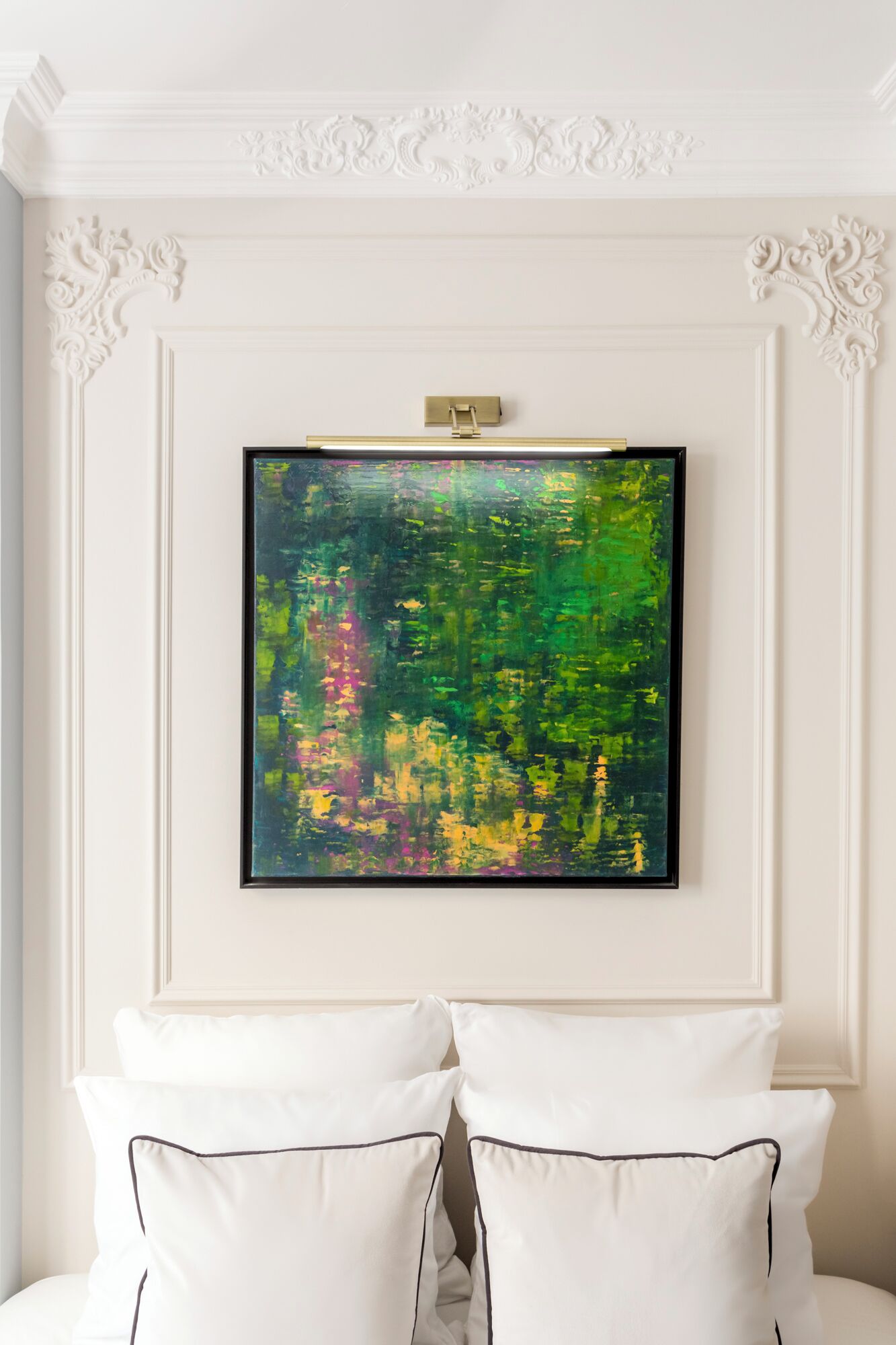 A framed abstract painting on a white wall above a bed with white pillows.
