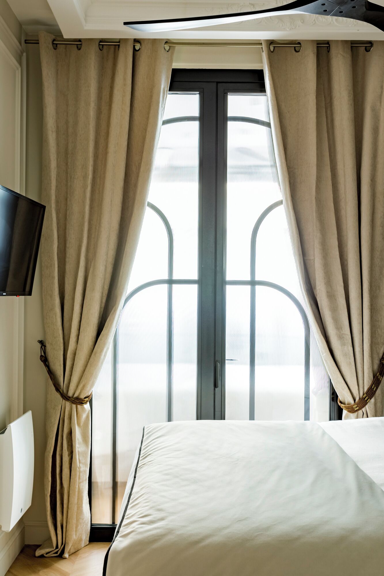 A hotel room with a bed, curtains, a television, and a view through a window.