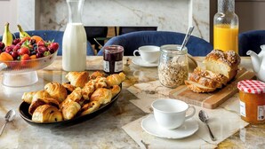 Egy márványasztalon tálalt reggeli, melynek része a croissant, gyümölcs és különböző italok, egy kandallóval és modern berendezéssel rendelkező szobában.