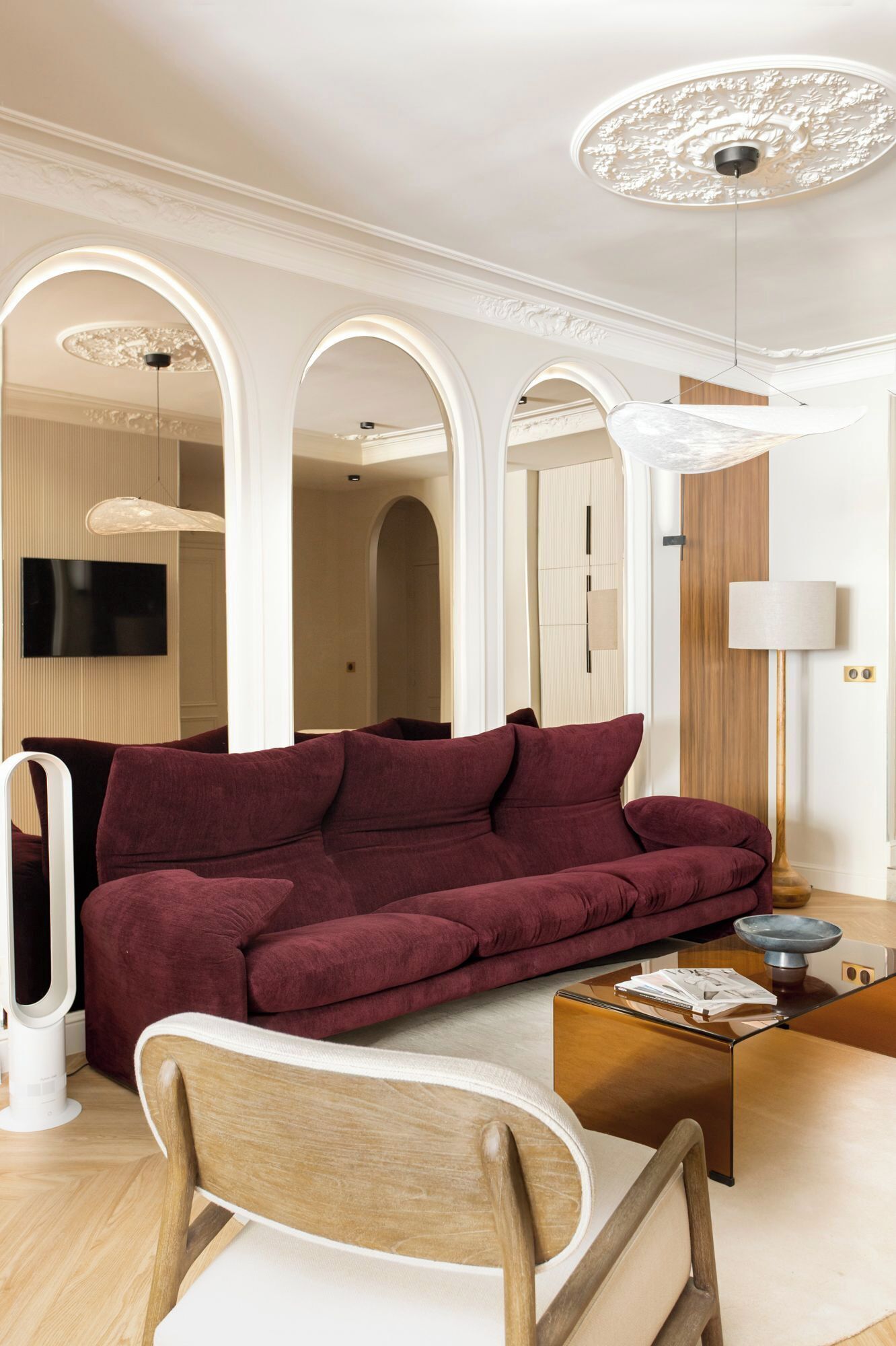 A modern living room with a red sofa, a wooden chair, a glass coffee table, and a TV mounted on the wall.