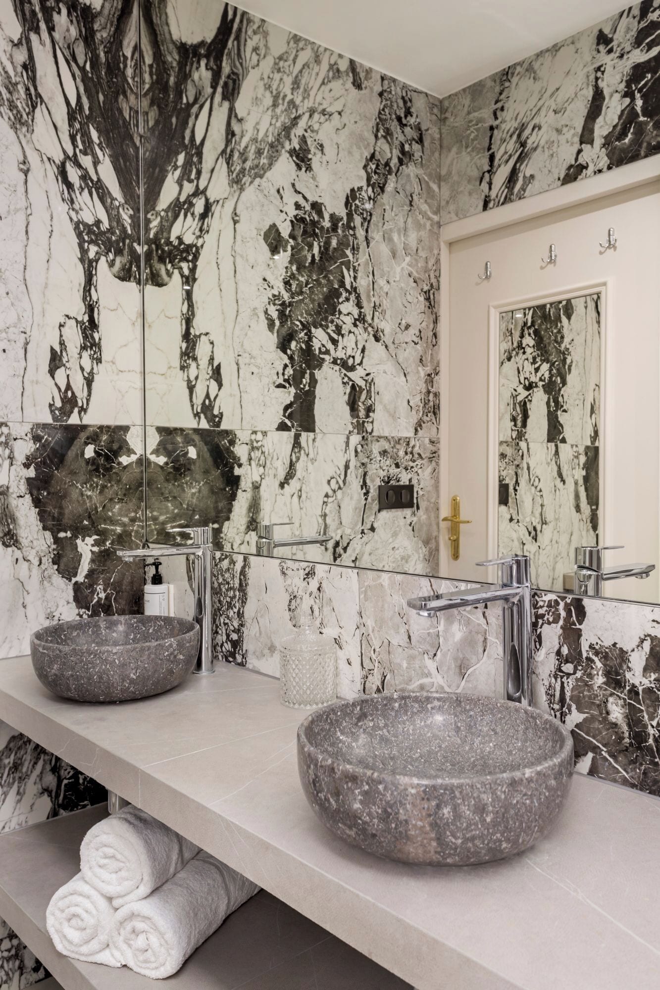 A bathroom with two stone sinks, a large mirror, and marble walls.