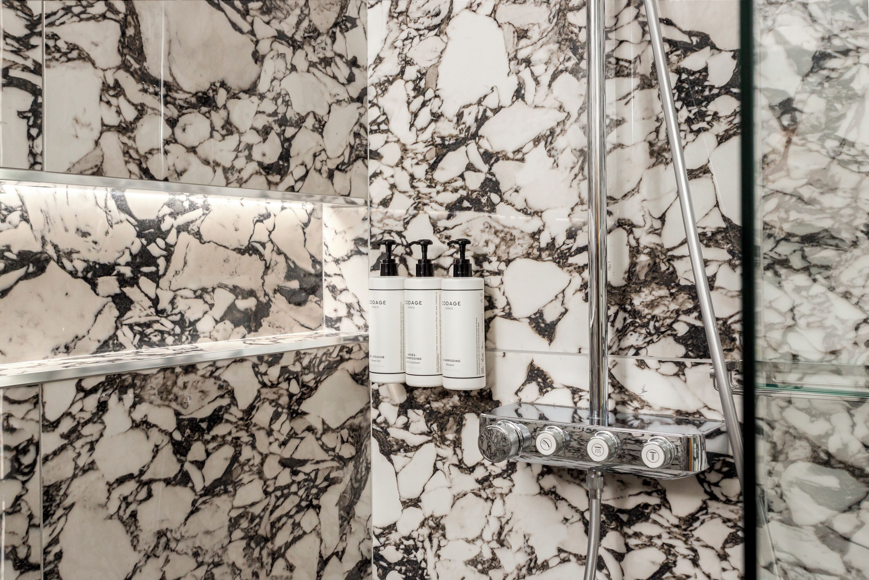 A bathroom with a marble wall, a glass shower enclosure, and a set of toiletries.