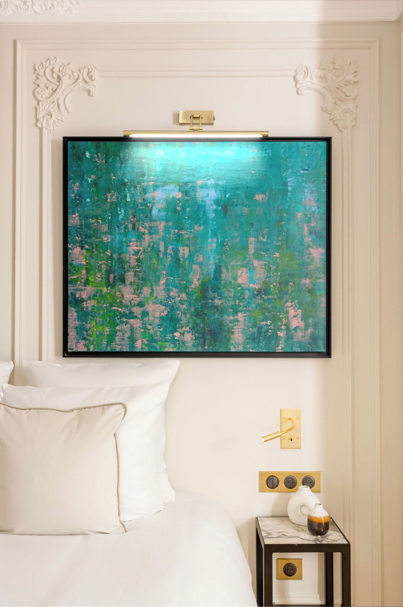 A hotel room with a large abstract painting on the wall, a bed with white linens, a bedside table with a vase and a glass, and a wall-mounted light fixture.