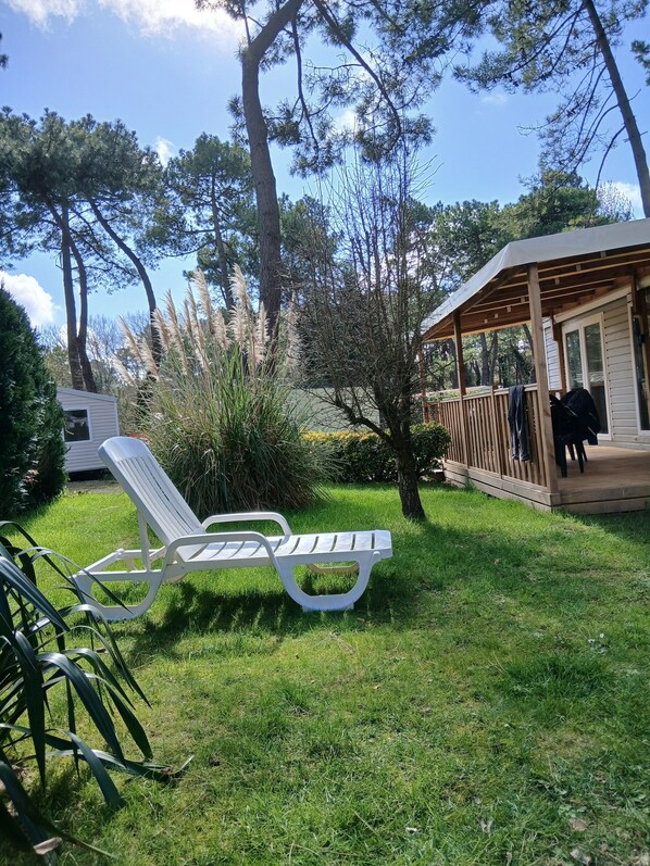 A grassy outdoor area with a white lounge chair, a wooden deck, and a covered structure.