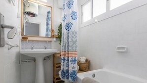 Ein Badezimmer mit einem Standwaschbecken, einem Spiegel, einer Duschvorhang, einer Badewanne und einem kleinen Holzboden mit Handtüchern.