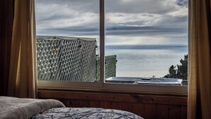 Une chambre dotée d’une grande fenêtre donnant sur la mer, d’un lit en bois et offrant une vue sur l’océan à travers un treillis.