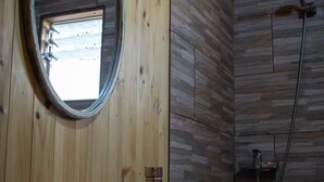 Une salle de bain rustique, avec une cabine en bois, un lavabo rectangulaire, un miroir rond et un espace douche.