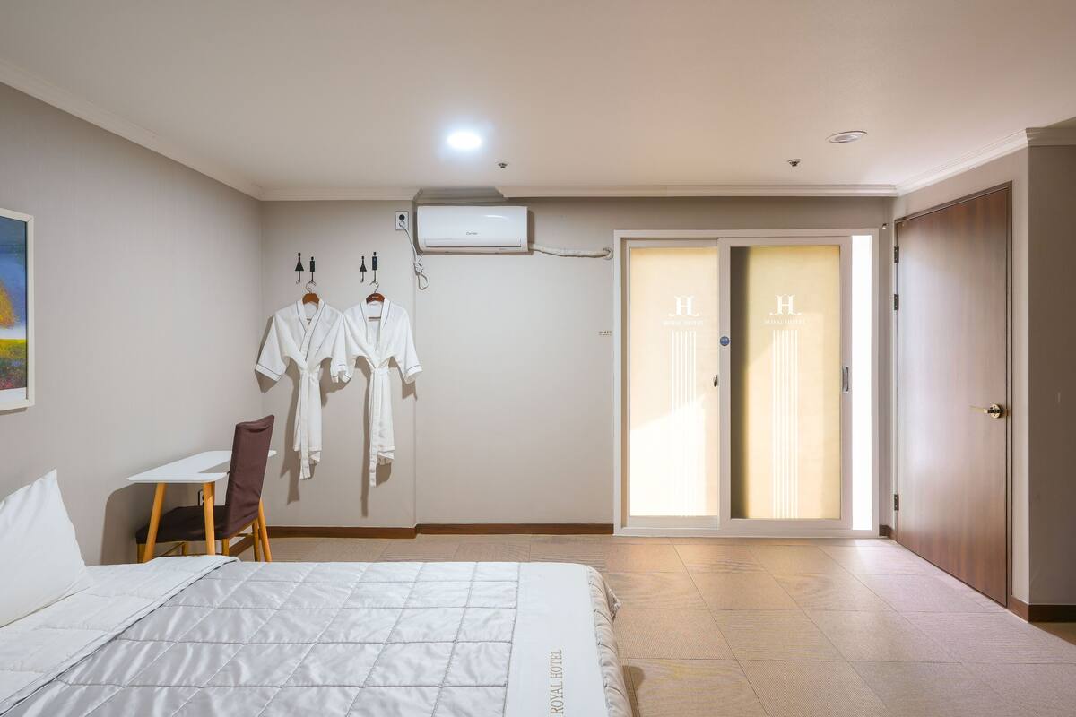 A hotel room with a bed, a desk, and a chair. There is a robe and towel rack on the wall.