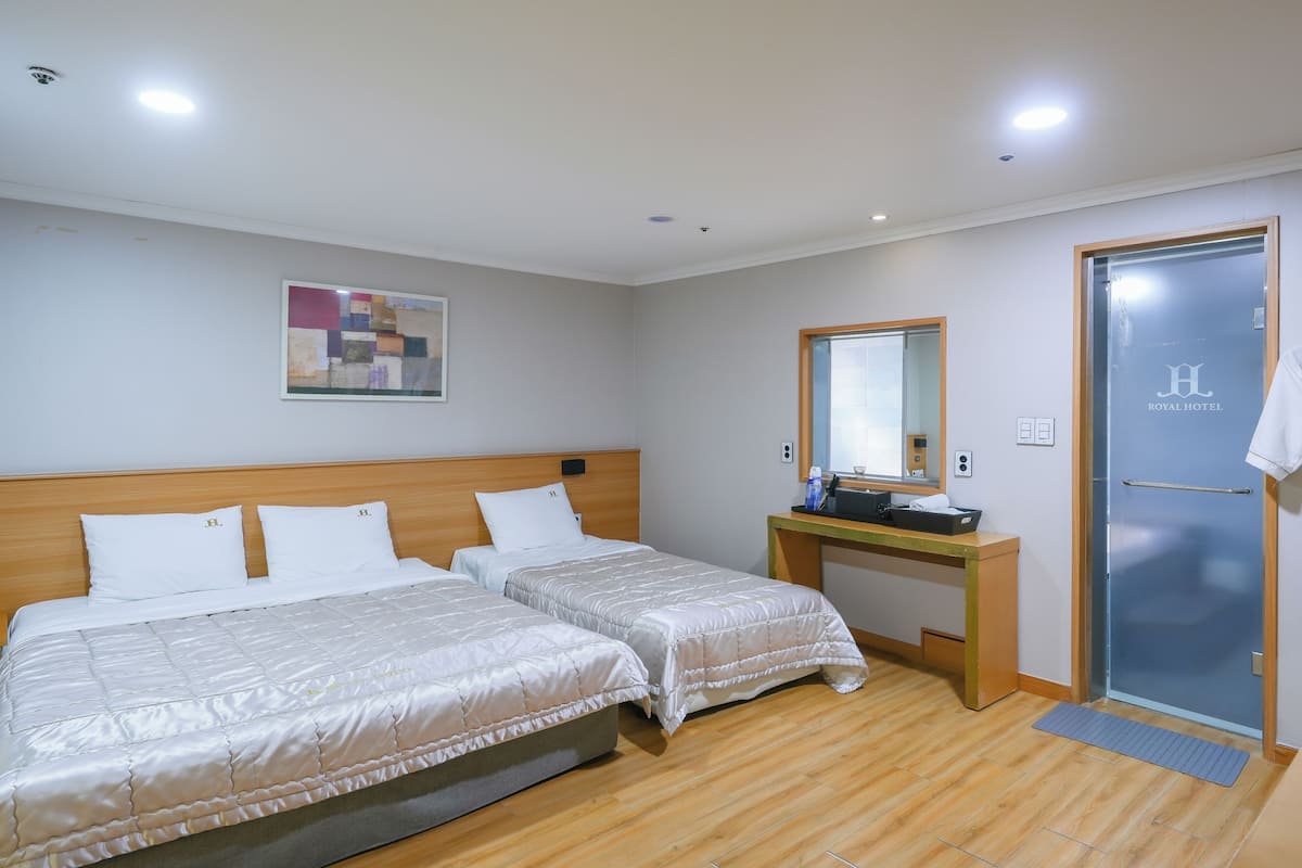 A hotel room with two beds, a desk, a mirror, and a door.