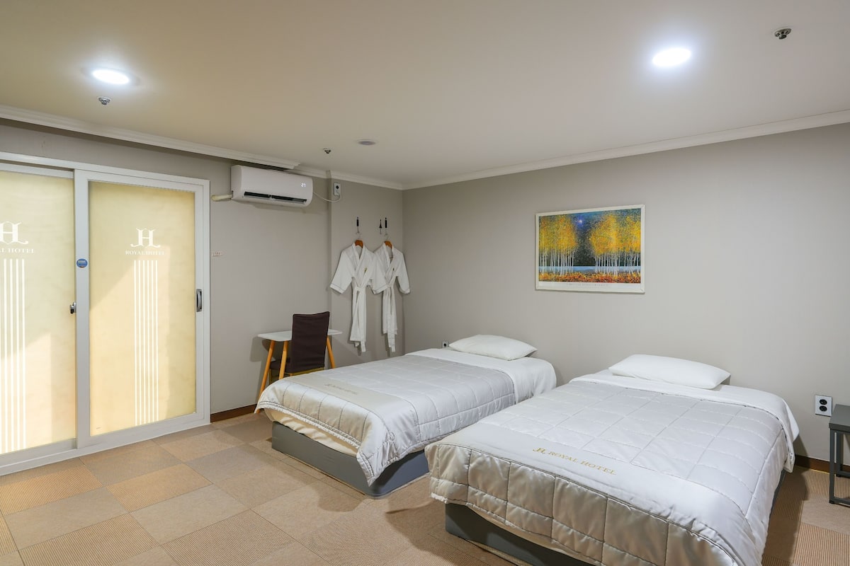 A hotel room with two beds, a sliding door, an air conditioning unit, and a painting on the wall.