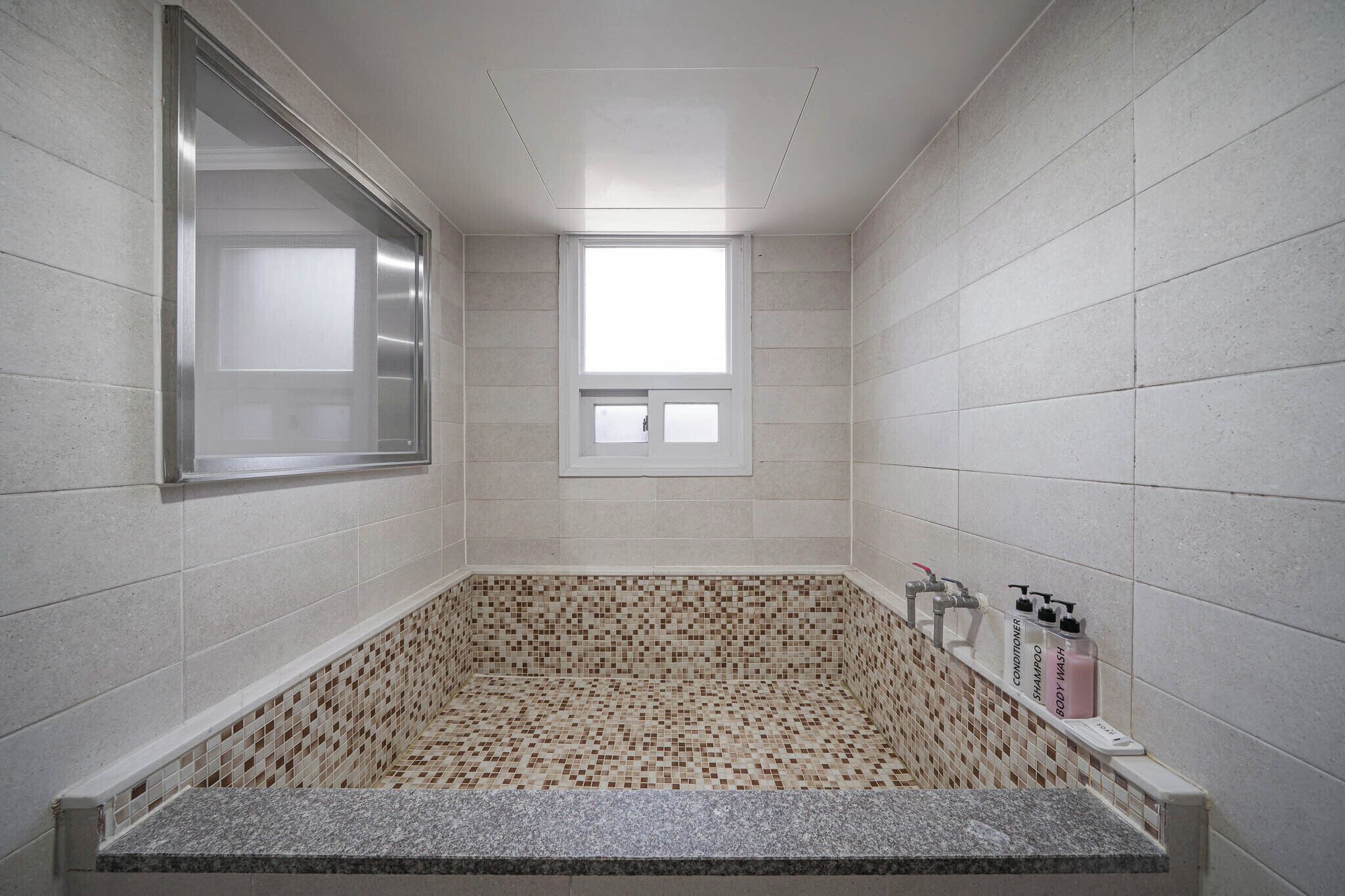 A modern bathroom with a mosaic tile floor, a built-in window, and a vanity with toiletries.