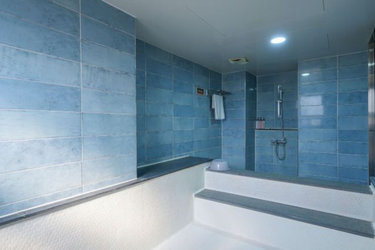 A modern bathroom with blue tiles, a white bathtub, and a shower area.