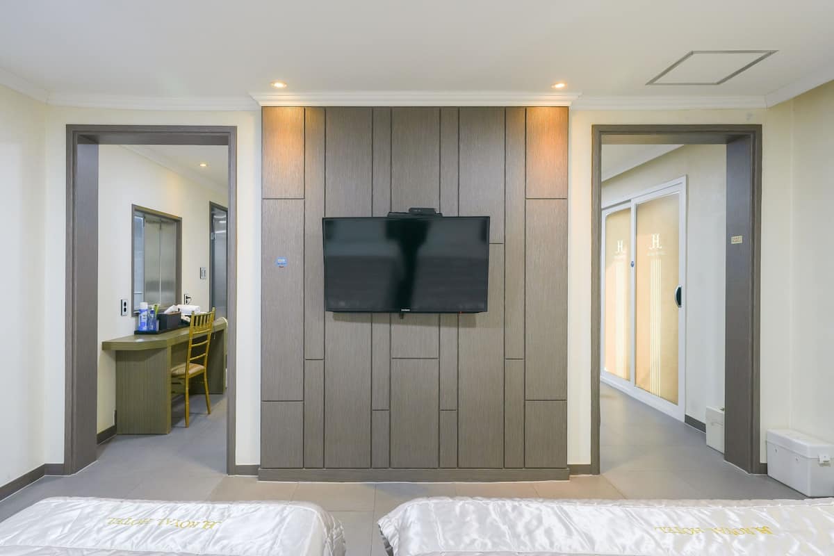 A hotel room with a flat-screen TV mounted on the wall, a desk with a chair, and two beds.
