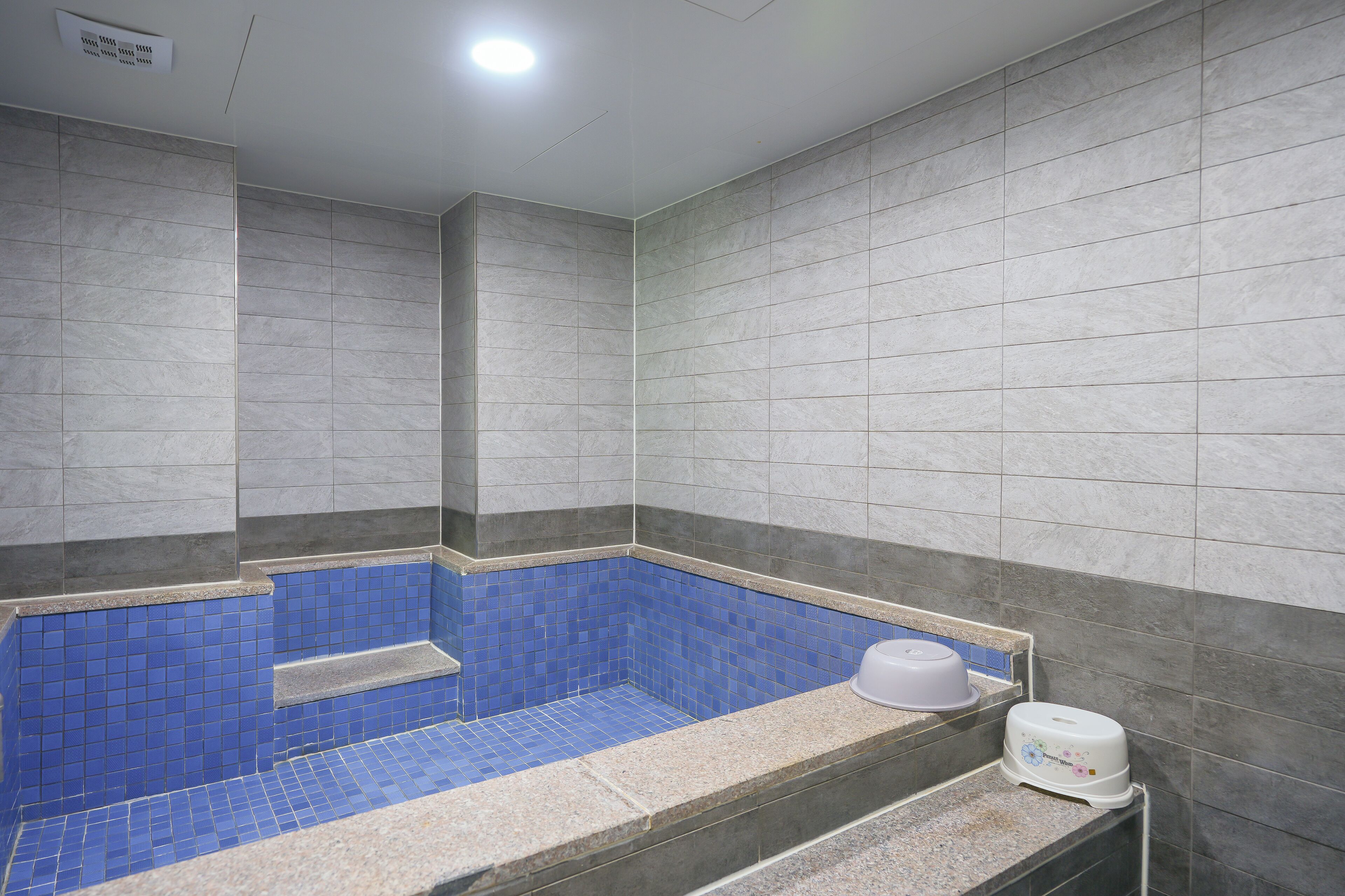 Une salle de bain avec une baignoire aux carreaux bleus, un lavabo blanc et un distributeur de serviettes.