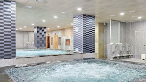 Una amplia piscina interior con un diseño de pared a cuadros, un área separada de hidromasaje y una zona de duchas con pared de azulejos.