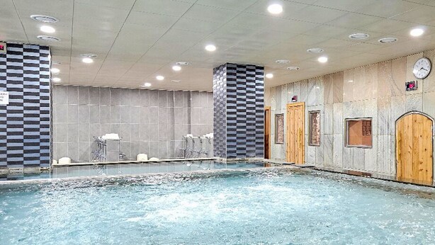 A large indoor swimming pool with multiple lanes, a checkered wall pattern, and a clock on the wall. - Bugok Royal Hotel (Changnyeong)