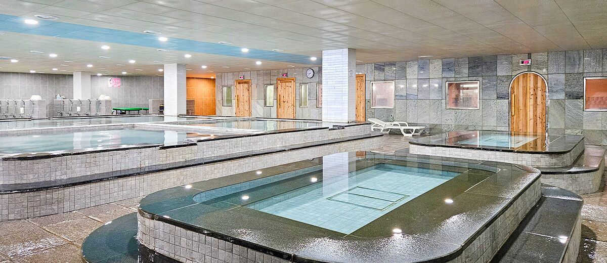A large indoor swimming pool with multiple lanes, a separate hot tub area, and a reception desk.