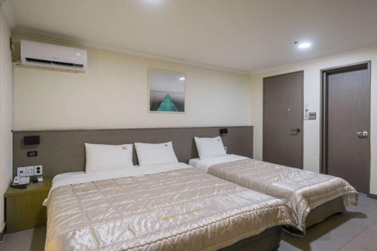 A hotel room with two beds, a wall-mounted air conditioner, a small picture, and a door.