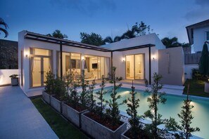 Une maison moderne dotée d’une piscine, de grandes fenêtres et d’un espace patio.