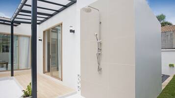 Een moderne badkamer met een douche, een glazen deur naar een terras en een potplant.