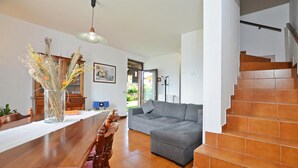 A dining area with a wooden table and chairs, a grey sofa, and a staircase with orange tiles. - Casa Lina (Colico)