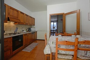 A kitchen with wooden cabinets, a dining table with chairs, and a view into the dining area. - Oasi E Relax (Colico)