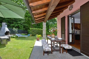 An outdoor patio with a wooden pergola, a barbecue grill, a dining table with benches, and a potted plant.