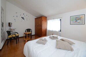 Une chambre d’hôtel avec un lit, une armoire en bois, une petite table avec une chaise et une fenêtre avec des rideaux.