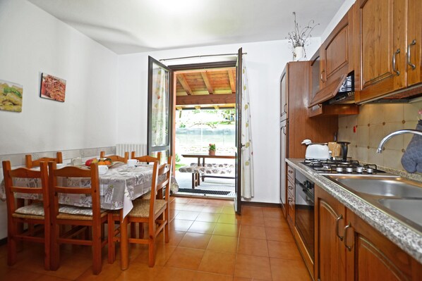 A kitchen with wooden cabinets, a sink, and a dining area with a table and chairs. - Oasi E Relax (Colico)