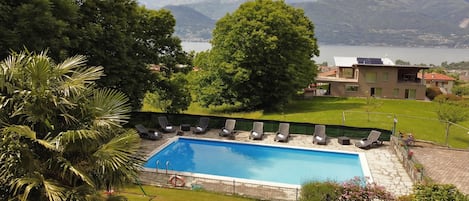 A swimming pool with lounge chairs, surrounded by greenery and a view of mountains.