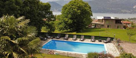 A swimming pool with lounge chairs, surrounded by greenery and a view of mountains.