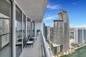 A balcony with a view of a modern high-rise building, a body of water, and other surrounding high-rises.