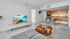 Una sala de estar moderna con un televisor de pantalla plana, una mesa de centro de madera y un comedor con cocina al fondo.