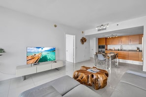 A modern living room with a flat-screen TV, a wooden coffee table, and a dining area with a kitchen in the background.