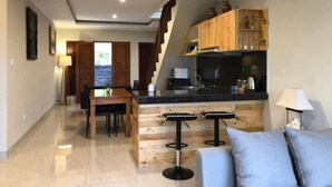 A modern kitchen with wooden cabinets, a dining area with a table and chairs, and a staircase leading to another level.