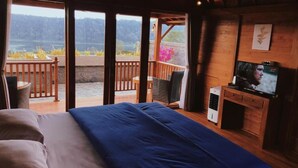 A bedroom with a bed, a television, and a view of a balcony with a wooden railing.