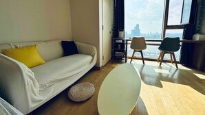 Un salon moderne avec un canapé, une table ronde et deux chaises. Une grande fenêtre offre une vue sur le paysage urbain.