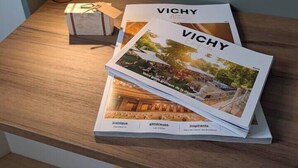 Una mesa de madera con una revista titulada 'VICHY' y una pequeña caja con un par de gafas encima.
