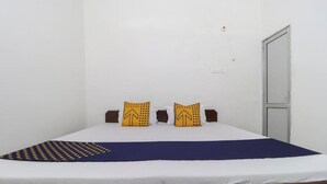 Una cama individual con colchón blanco y colcha azul, dos almohadas con estampado amarillo, y cabecera marrón.