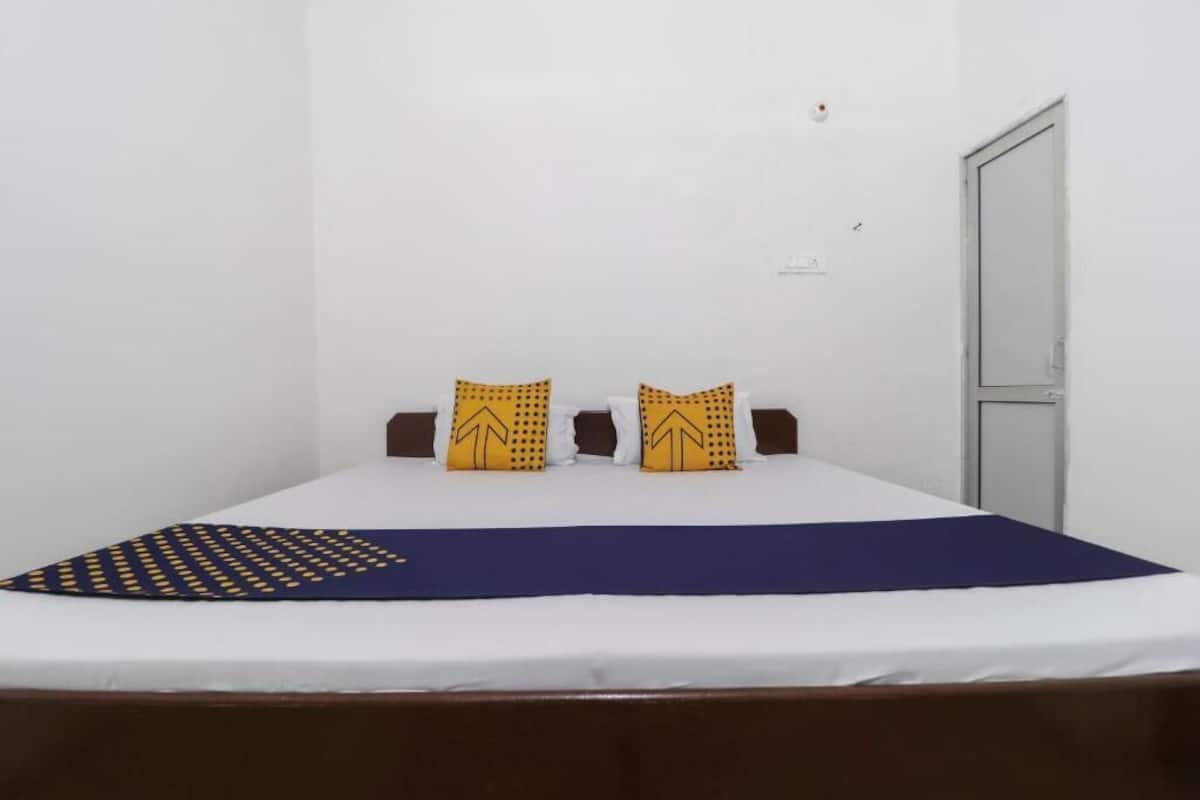 A single bed with a white mattress and a blue bedspread, two pillows with a yellow pattern, and a brown headboard.