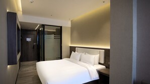Une chambre d’hôtel moderne dotée d’un grand lit, d’une table de chevet, d’un bureau et d’une porte coulissante donnant accès à la salle de bain.