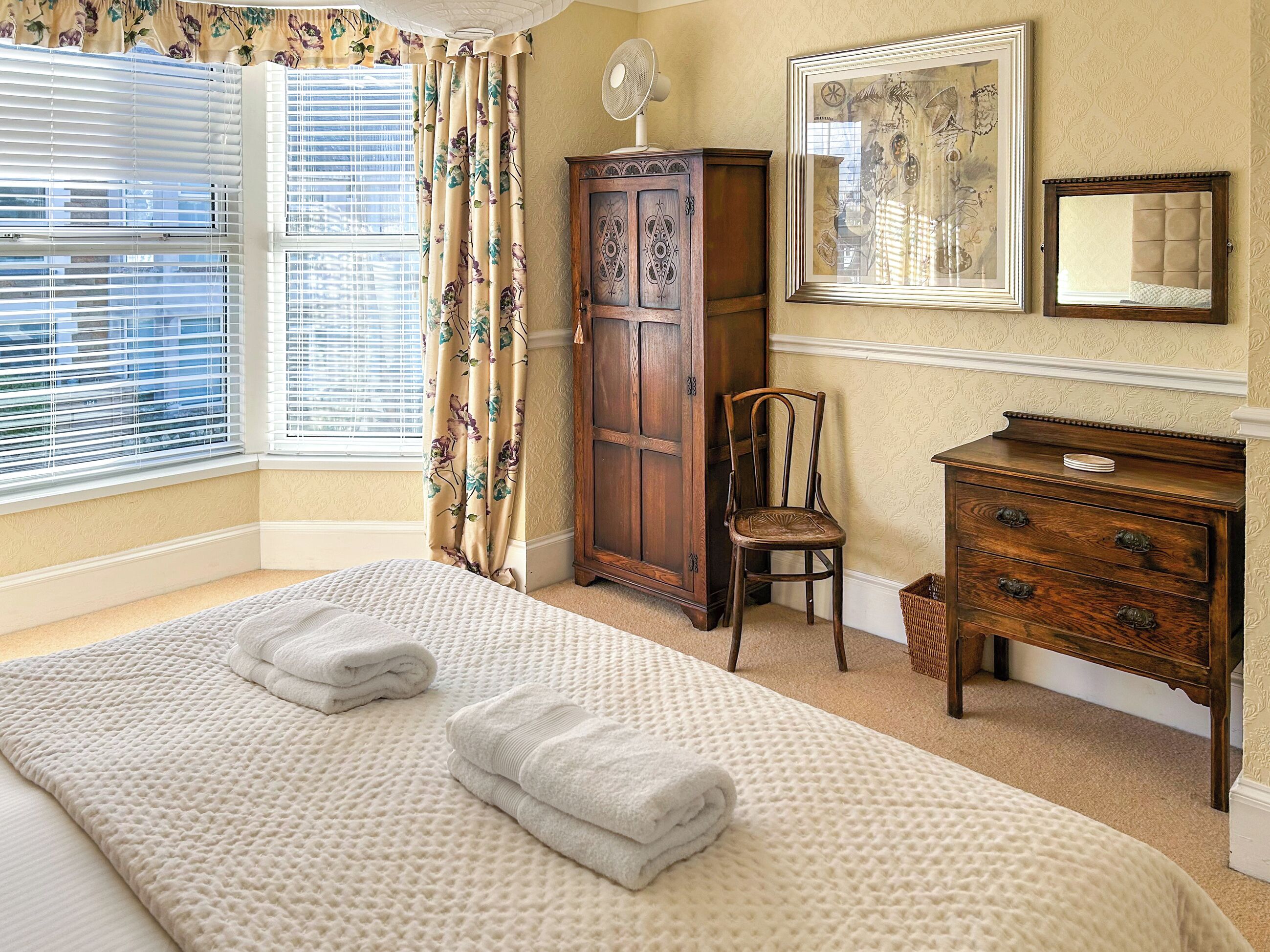 A bedroom with a large bed, a wooden wardrobe, a chair, and a dresser.