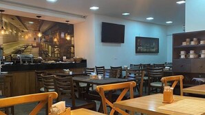 A restaurant with wooden tables and chairs, a counter with a coffee machine, and a flat-screen TV on the wall. - HOTEL GUARULHOS  (Guarulhos)