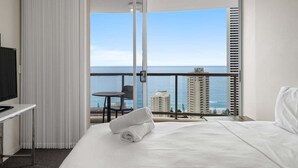 Une chambre d’hôtel avec un lit, une télévision, un bureau et une vue sur l’océan et les bâtiments.