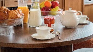 A breakfast setup with croissants, fruit, milk, and tea on a wooden table in a kitchen with marble countertops and wooden cabinets. - Merveil Luxury Suites - Bourse I-II (Paris)
