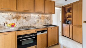 A modern kitchen with wooden cabinets, a marble backsplash, a built-in oven, and a dishwasher. - Merveil Luxury Suites - Bourse I-II (Paris)