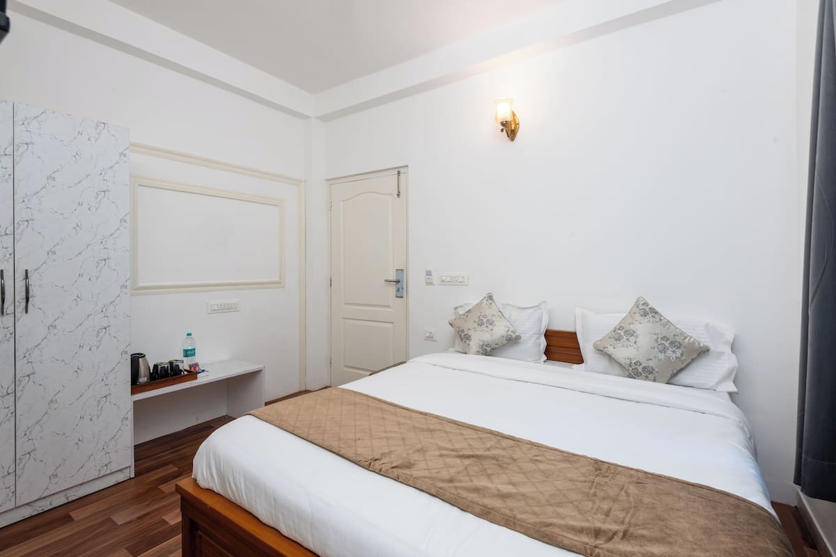 A hotel room with a bed, a wardrobe, a bedside table, and a wall-mounted light fixture.