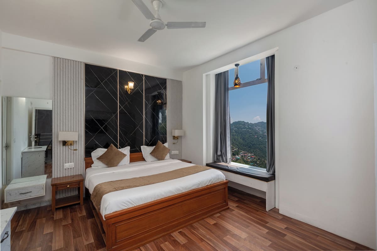 A modern bedroom with a large bed, a ceiling fan, a window with a view, and a nightstand with a lamp.